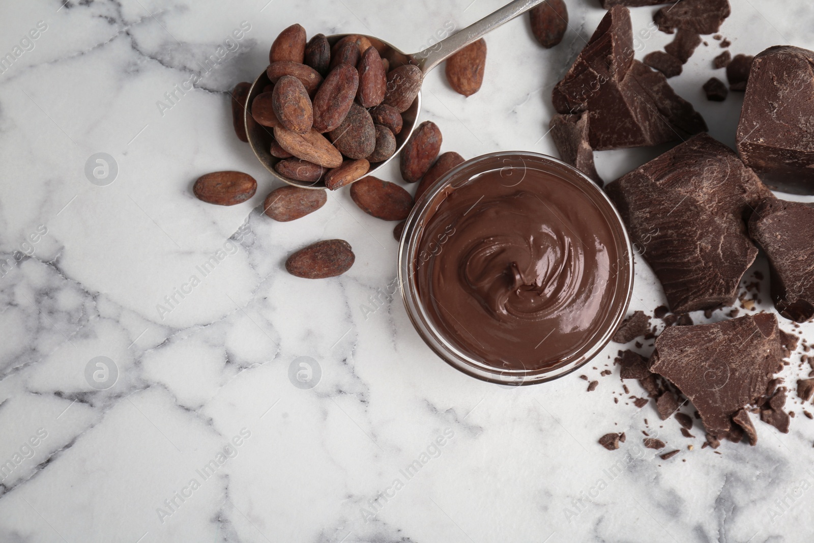 Photo of Bowl with tasty melted chocolate, chunks and cocoa beans on table, top view