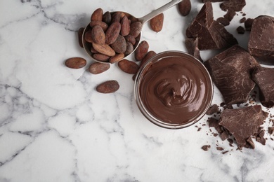 Bowl with tasty melted chocolate, chunks and cocoa beans on table, top view