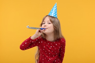 Cute little girl in party hat with blower on yellow background