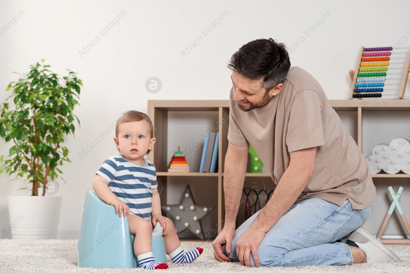 Photo of Father training his child to sit on baby potty indoors