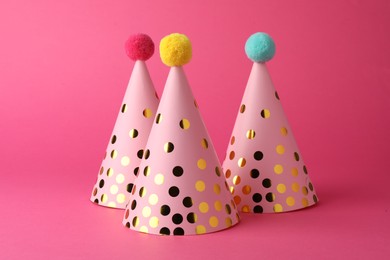 Photo of Beautiful party hats with pompoms on pink background