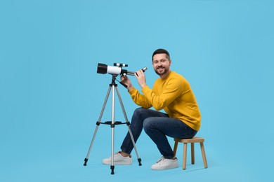 Photo of Happy astronomer with telescope on light blue background