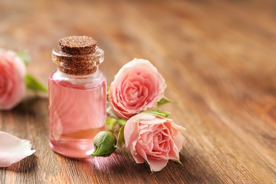 Photo of Bottle of rose essential oil and flowers on wooden table, space for text