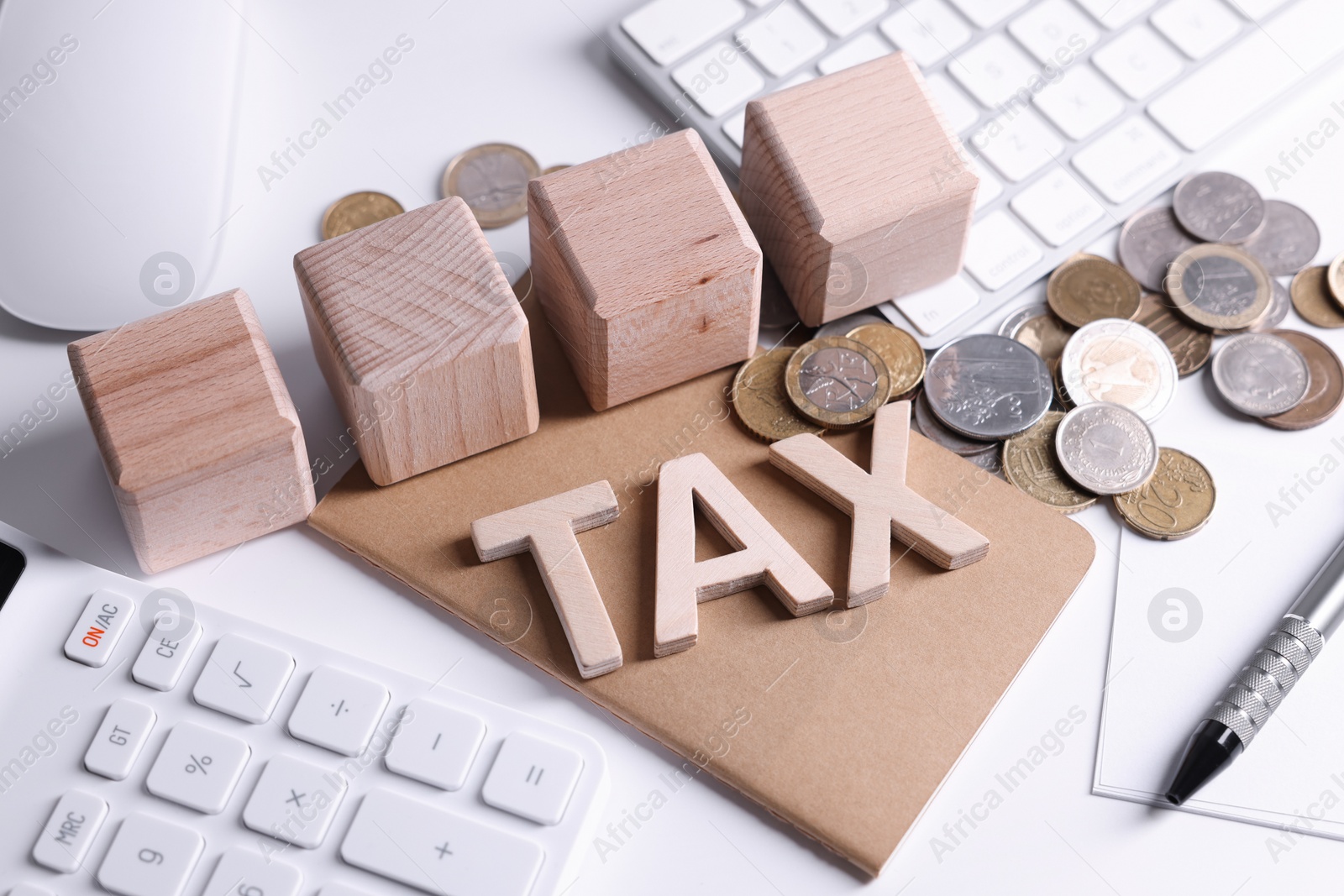 Photo of Word Tax, wooden cubes, calculator, coins, keyboard and pen on white table