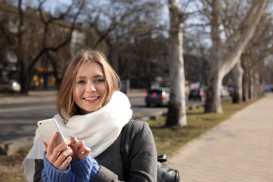 Photo of Portrait of happy young woman using phone outdoors on sunny day