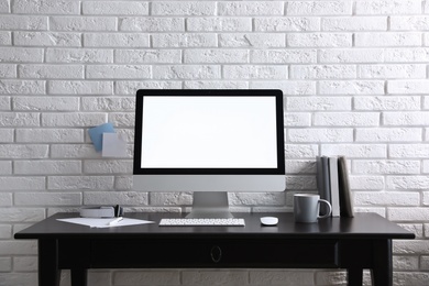 Photo of Comfortable workplace with modern computer on black table near white brick wall. Space for text