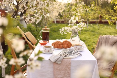 Photo of Stylish table setting with beautiful spring flowers, tea and croissants in garden