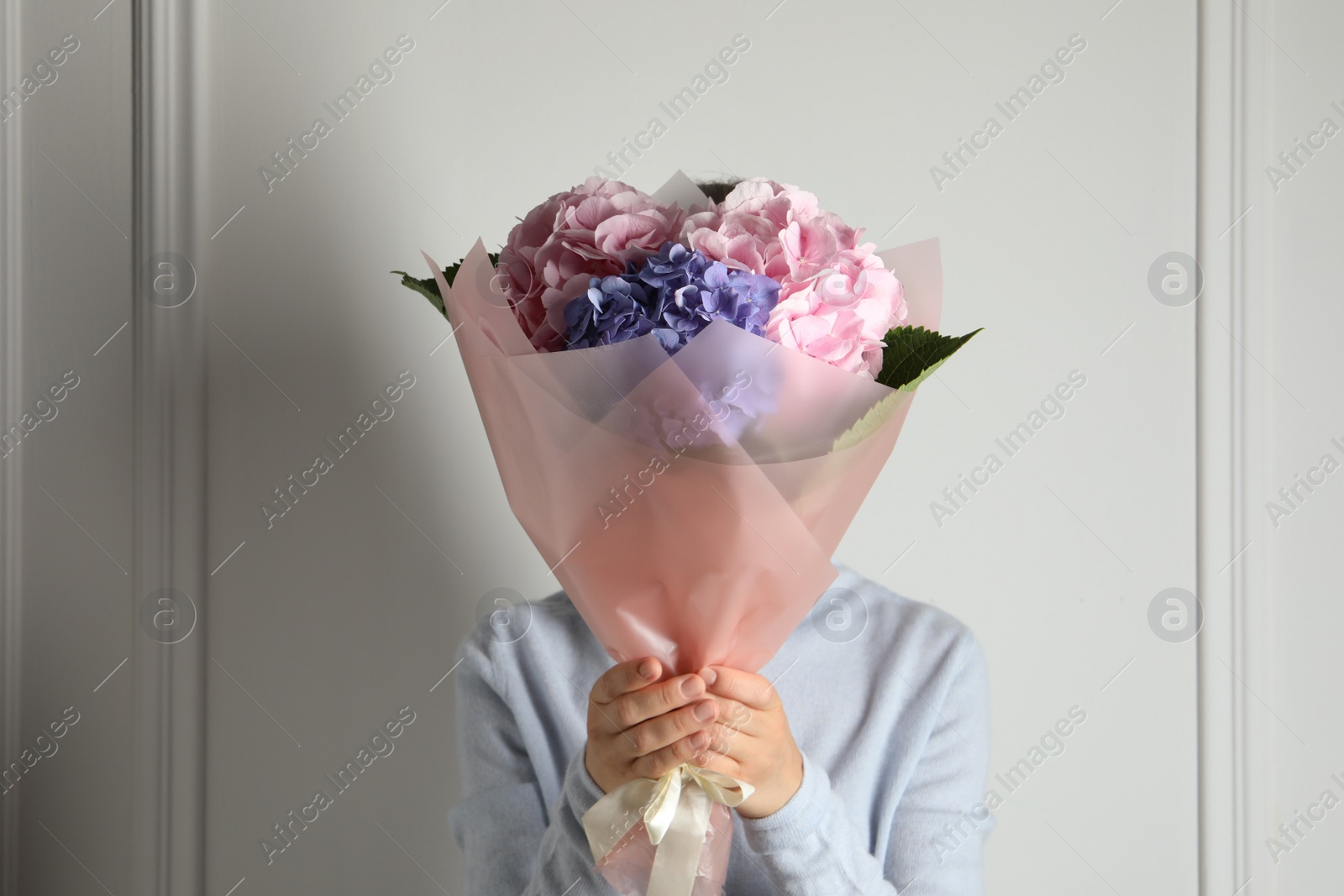 Photo of Woman with bouquet of beautiful hortensia flowers near white wall