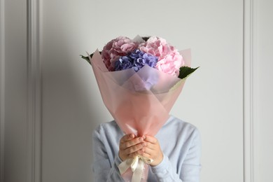 Photo of Woman with bouquet of beautiful hortensia flowers near white wall