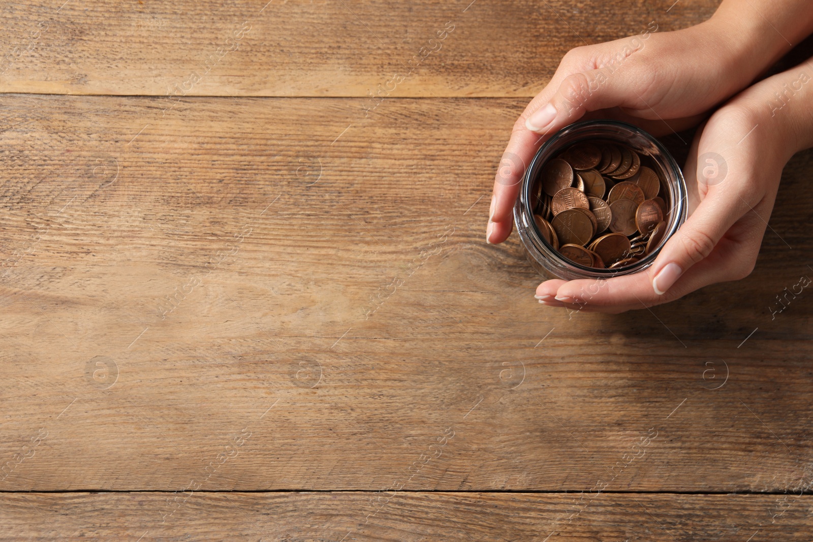 Photo of Woman holding glass jar with coins on wooden table, closeup. Space for text