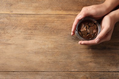 Woman holding glass jar with coins on wooden table, closeup. Space for text