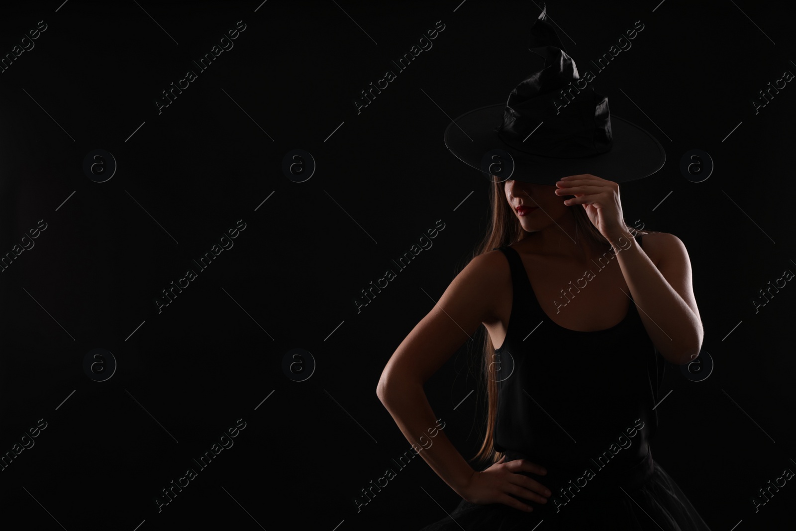 Photo of Young woman wearing witch costume on black background, space for text. Halloween party