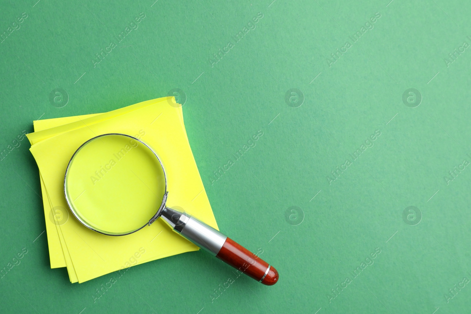 Photo of Magnifier glass and empty paper sheets on green background, flat lay with space for text. Find keywords concept