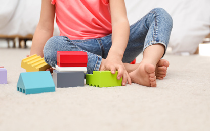 Photo of Cute child playing with building blocks on floor at home, closeup