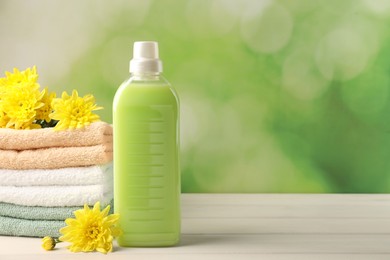 Photo of Bottle of laundry detergent, towels and beautiful flowers on white wooden table. Space for text