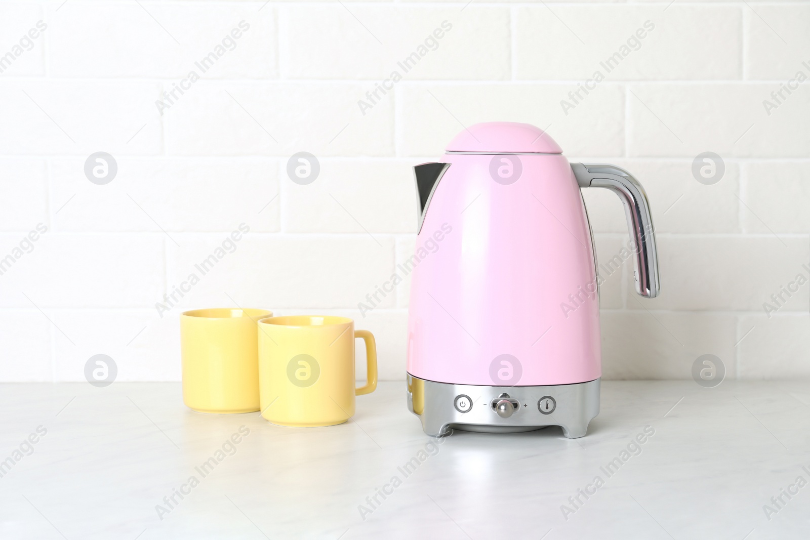 Photo of Modern electric kettle and cups on counter in kitchen