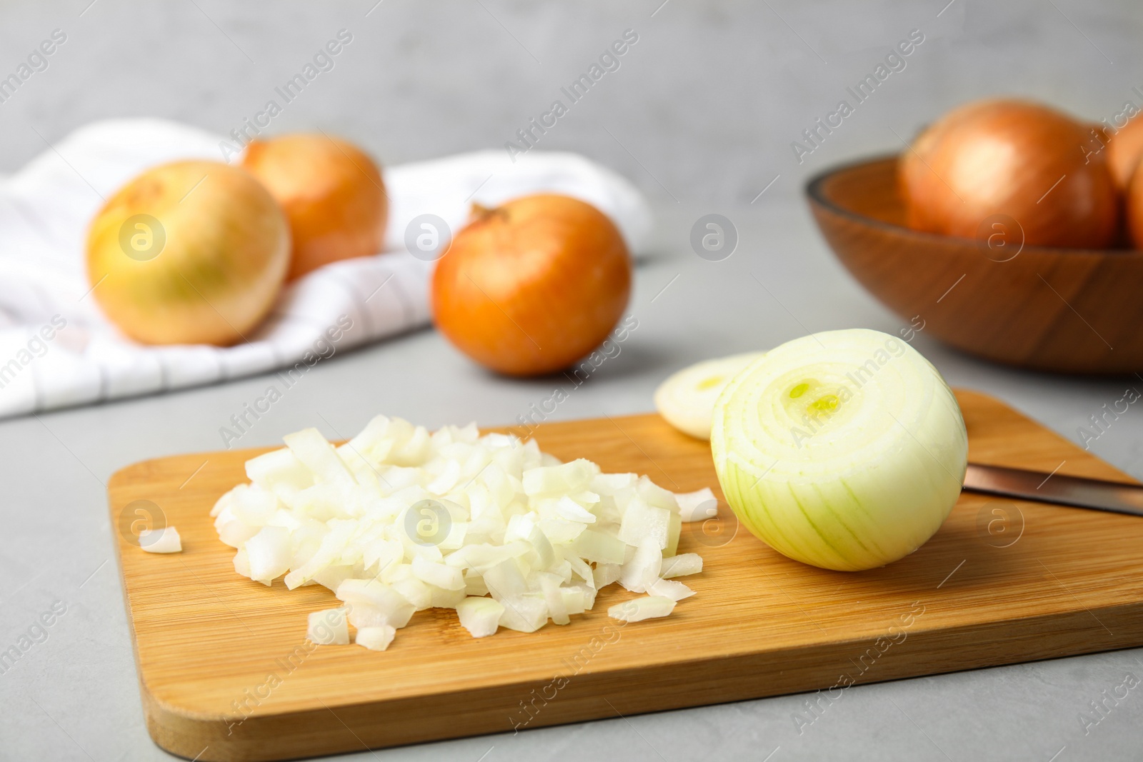 Photo of Wooden board with cut onion and knife on grey table