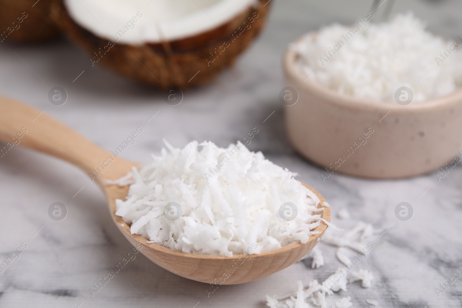 Photo of Coconut flakes in wooden spoon on white marble table, closeup