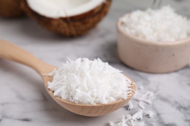 Coconut flakes in wooden spoon on white marble table, closeup