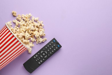 Photo of Remote control and cup of popcorn on violet background, flat lay. Space for text