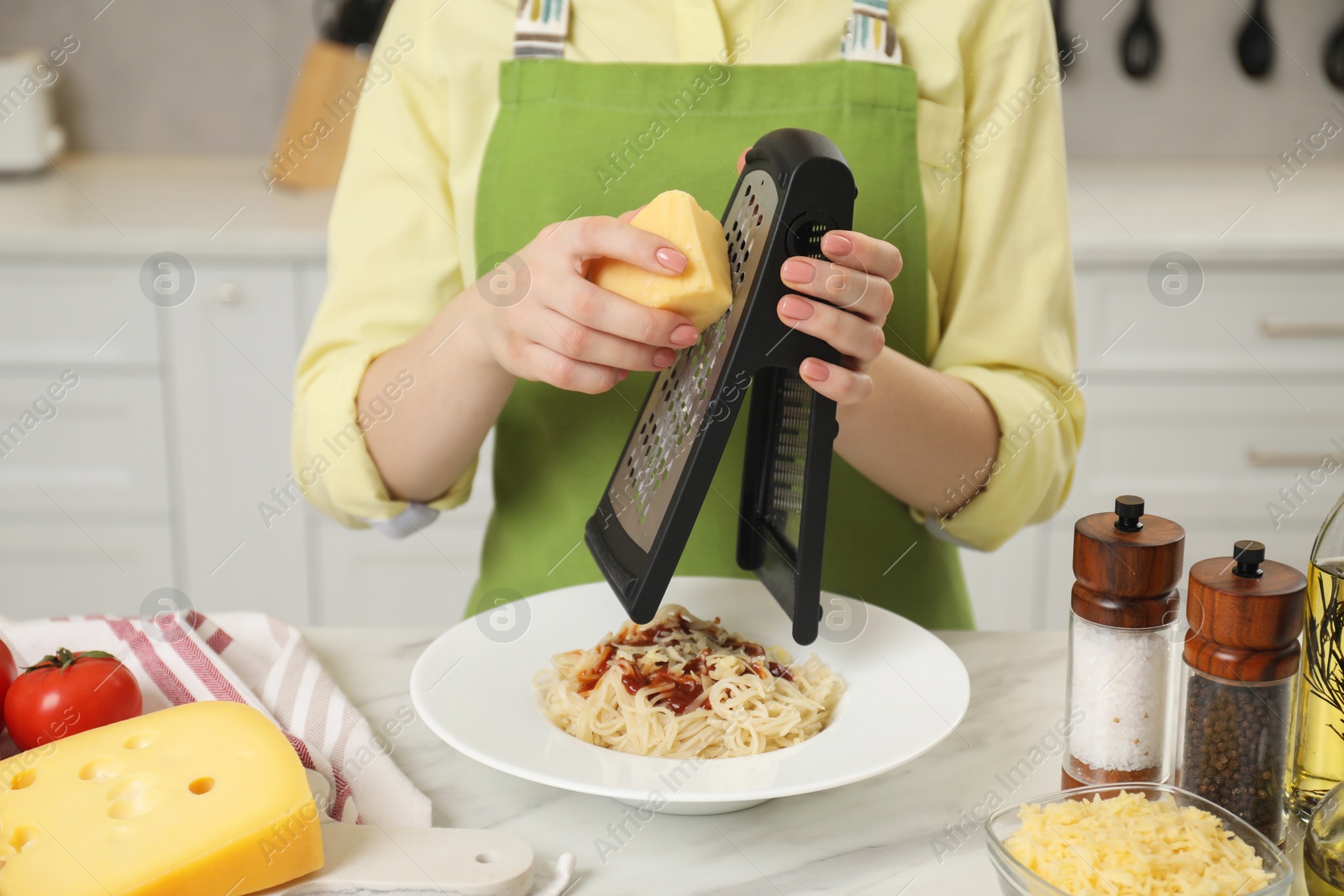 Photo of Woman grating cheese onto delicious pasta at white marble table in kitchen, closeup