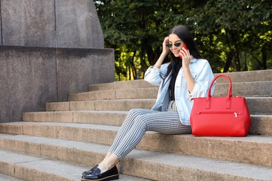 Young woman with stylish bag talking on phone outdoors, space for text