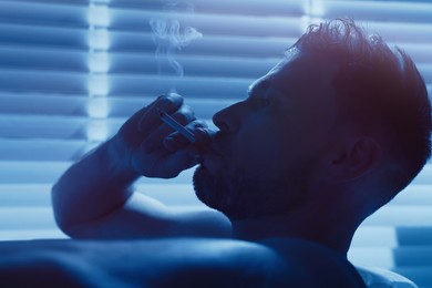 Photo of Upset man smoking in bathtub at night. Loneliness concept