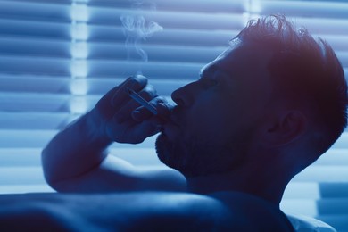 Upset man smoking in bathtub at night. Loneliness concept