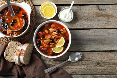 Photo of Meat solyanka soup with sausages, olives and vegetables served on wooden table, flat lay. Space for text