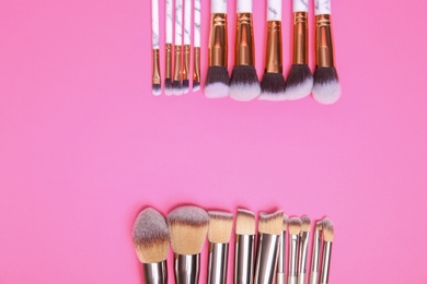 Flat lay composition with set of professional makeup brushes on pink background. Space for text