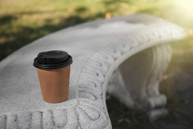 Cardboard cup with tasty coffee on stone bench outdoors. Space for text