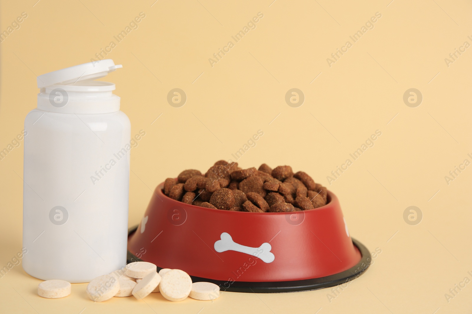 Photo of Bottle with vitamins and dry pet food in bowl on beige background