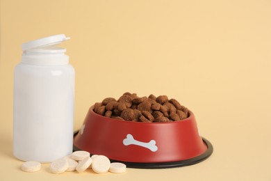 Photo of Bottle with vitamins and dry pet food in bowl on beige background