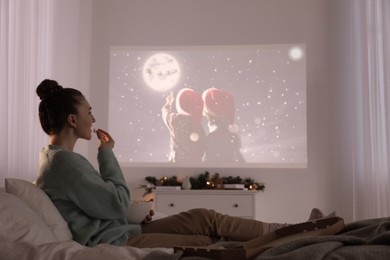 Woman with popcorn watching Christmas movie via video projector at home