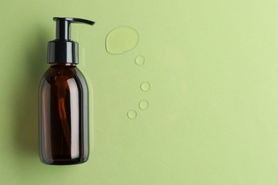 Photo of Bottle and drops of hydrophilic oil on light green background, flat lay. Space for text