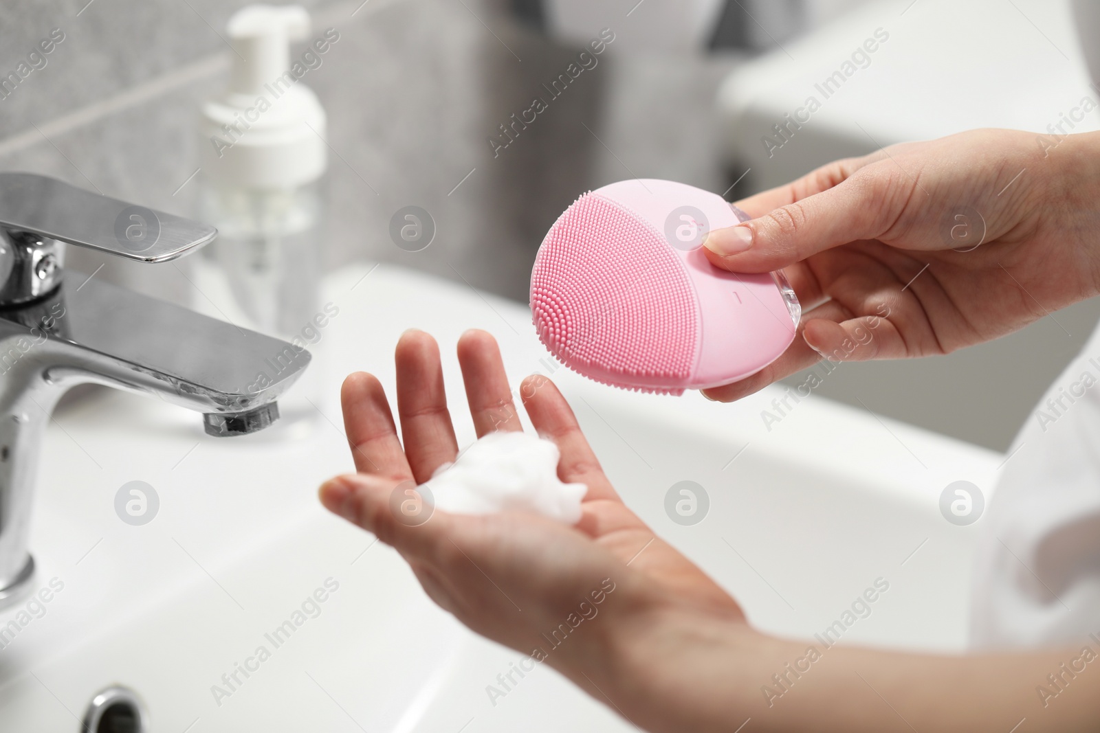 Photo of Washing face. Woman with brush and cleansing foam above sink in bathroom, closeup