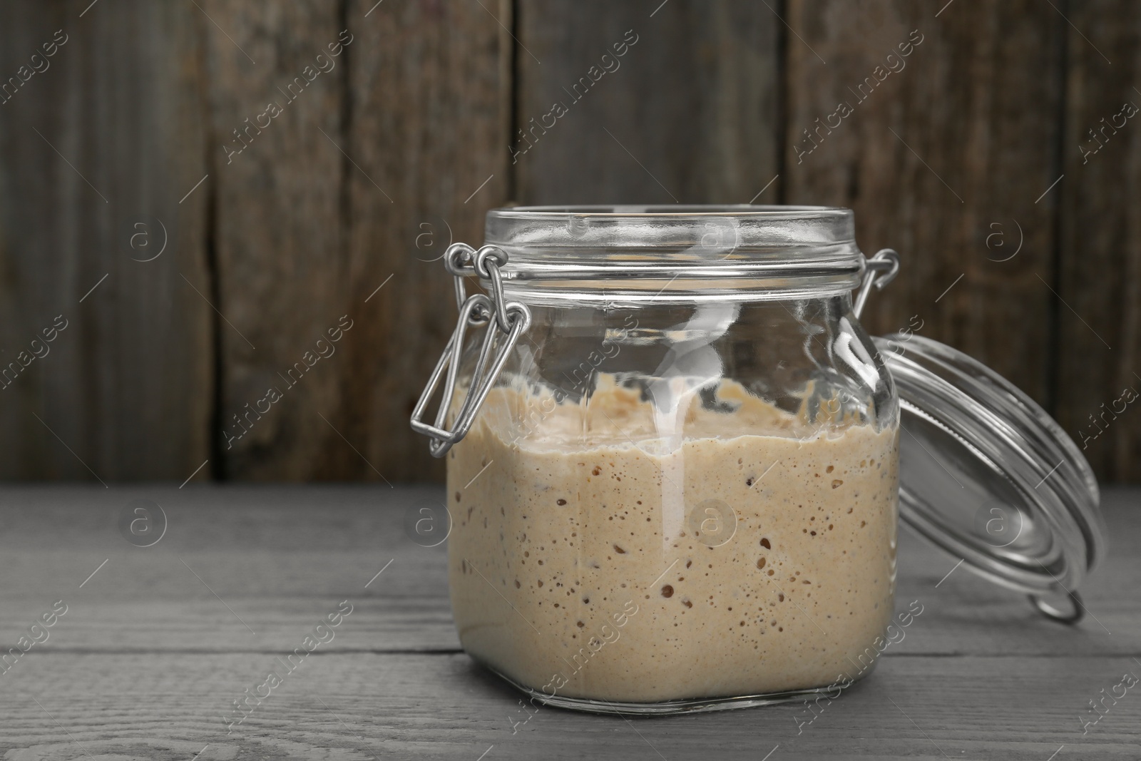 Photo of Leaven in glass jar on grey wooden table, space for text