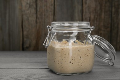 Photo of Leaven in glass jar on grey wooden table, space for text