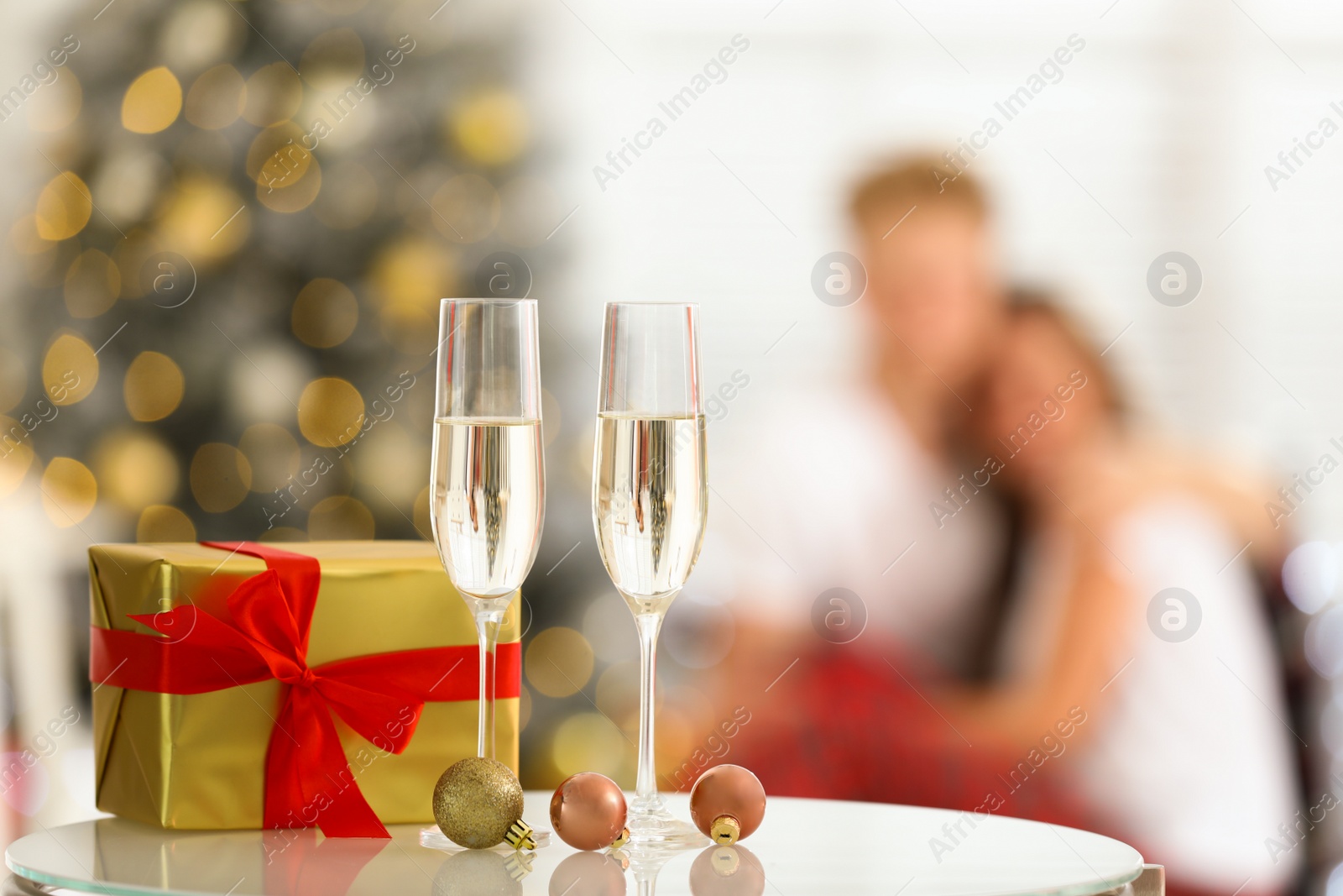 Photo of Christmas gift and glasses of champagne on table against blurred background