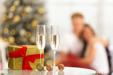 Photo of Christmas gift and glasses of champagne on table against blurred background