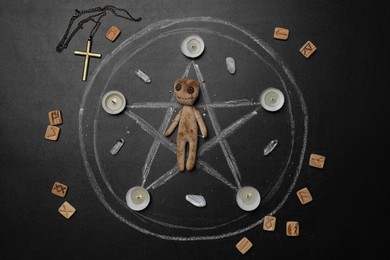 Voodoo doll with pins surrounded by ceremonial items on black table, flat lay