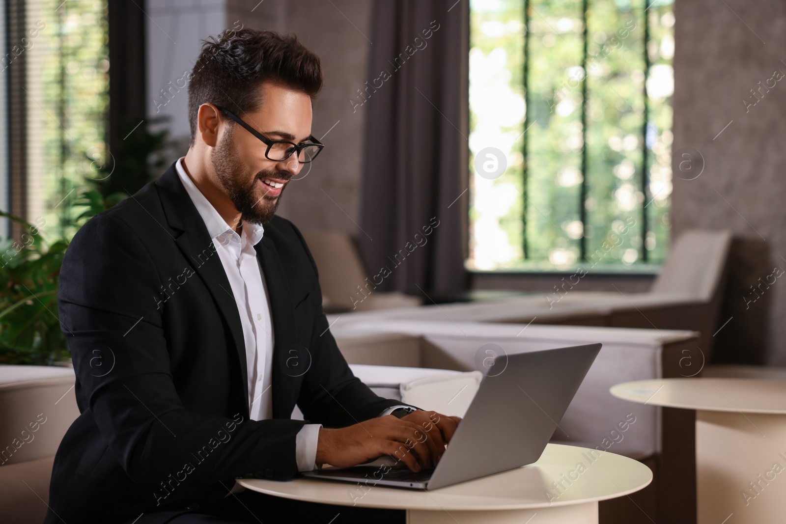 Photo of Happy young man with glasses working on laptop at table in office