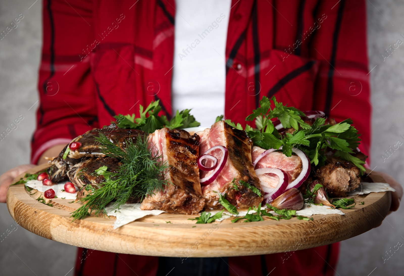 Photo of Woman holding wooden board with delicious roasted ribs and herbal on grey background, closeup