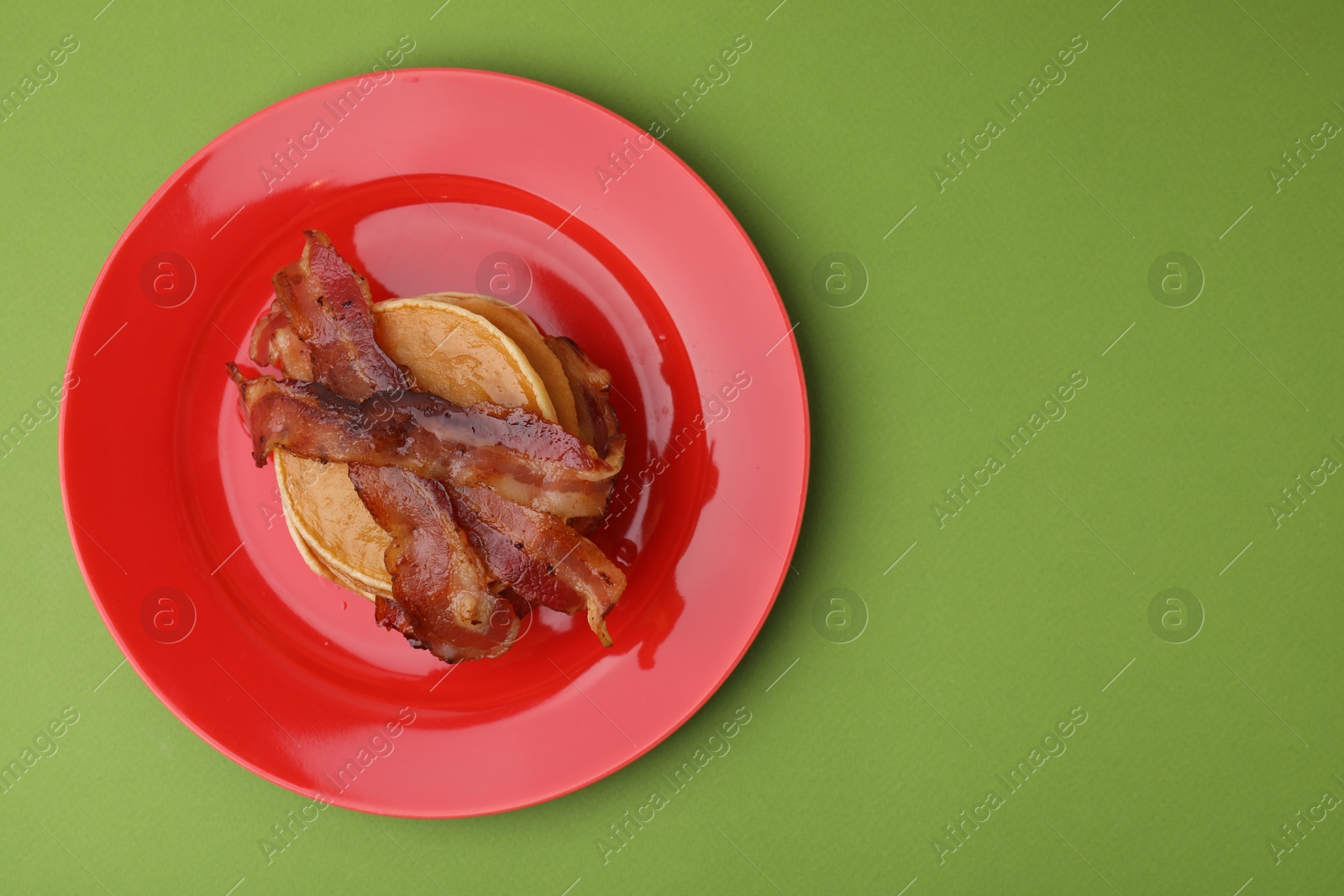Photo of Delicious pancakes with bacon on green table, top view. Space for text