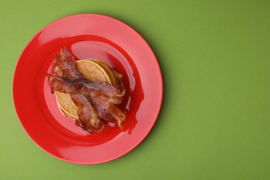Delicious pancakes with bacon on green table, top view. Space for text