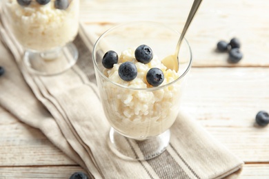 Photo of Creamy rice pudding with blueberries in dessert bowl on white wooden table