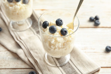 Creamy rice pudding with blueberries in dessert bowl on white wooden table