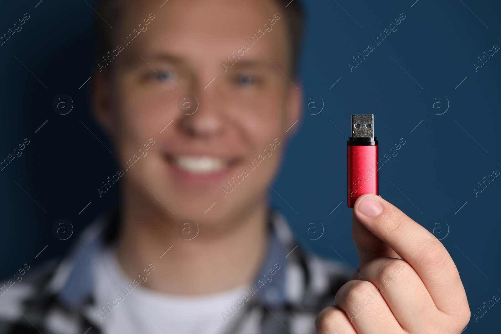 Photo of Man with usb flash drive against blue background, focus on device. Space for text