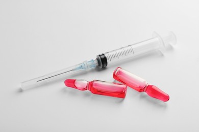 Photo of Glass ampoules with liquid and syringe on white background