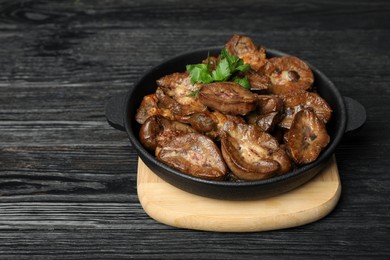 Frying pan with delicious kidneys and parsley on black wooden table, space for text